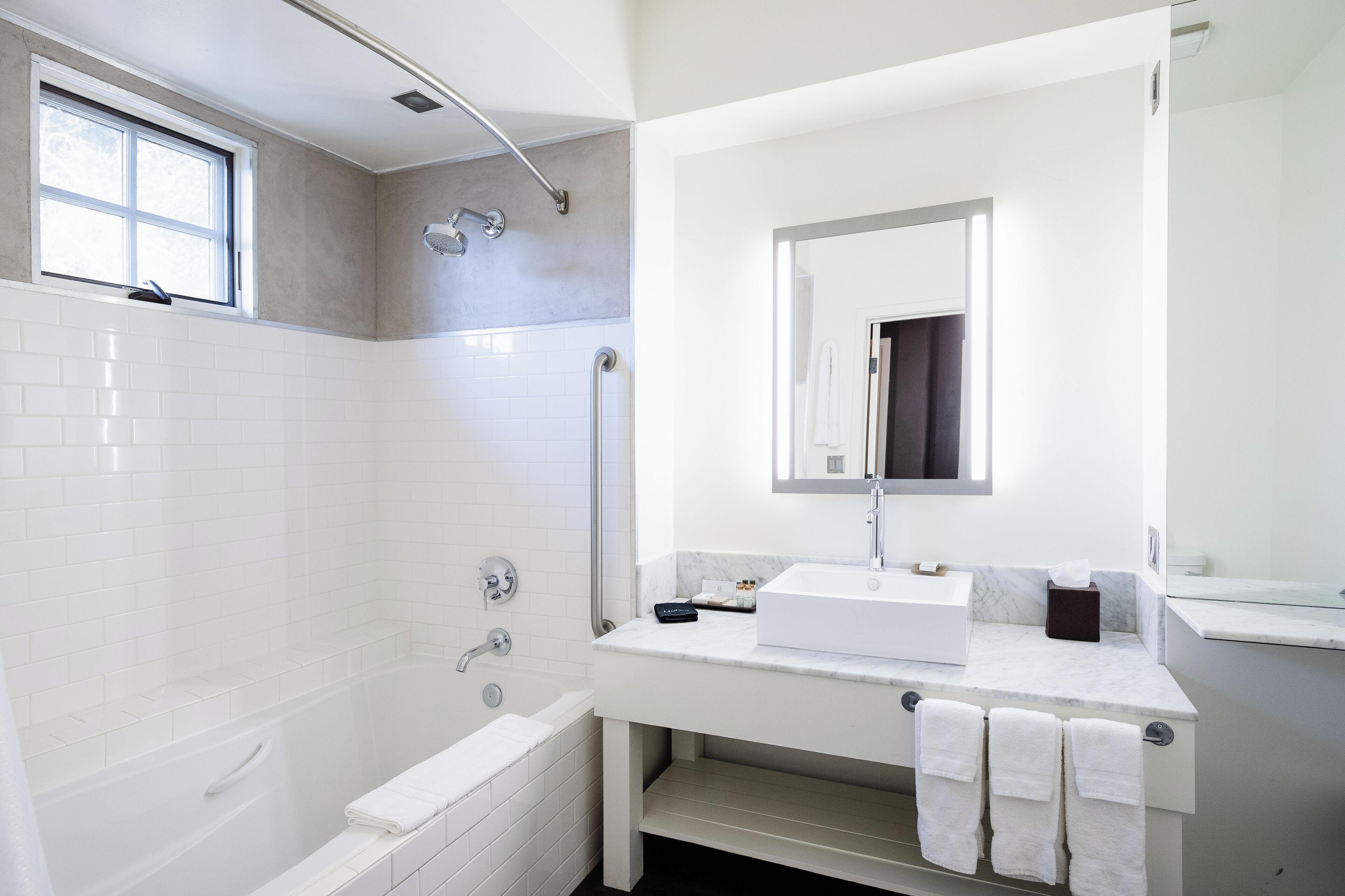 Un baño moderno con bañera, ducha, tocador con espejo y ventana.