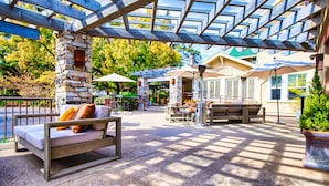 An outdoor patio area with a stone pillar, a wooden bench, and a cushioned seating area.