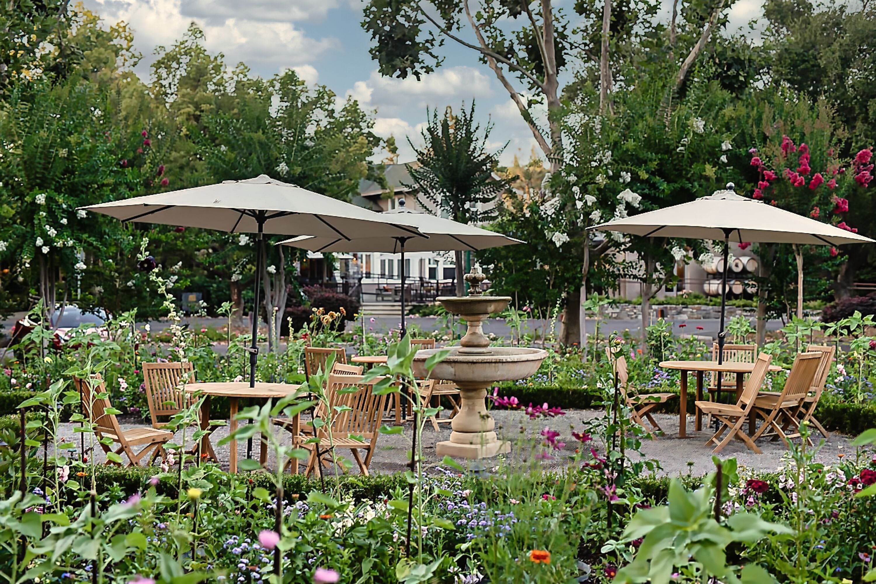 An outdoor seating area with wooden tables and chairs, surrounded by lush greenery and flowers.