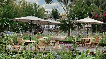 An outdoor seating area with wooden tables and chairs, surrounded by lush greenery and flowers.