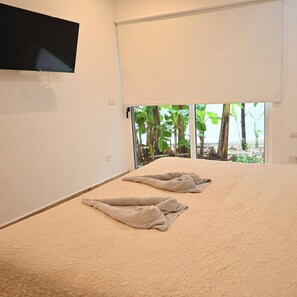 Una habitación con una cama, un televisor de pantalla plana montado en la pared y un ventanal corredero que da a vistas de vegetación.