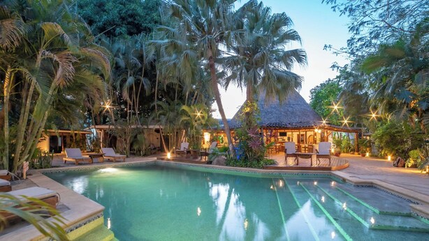 A pool area with lounge chairs and a thatched-roof structure. - Hotel Pasatiempo (Tamarindo)