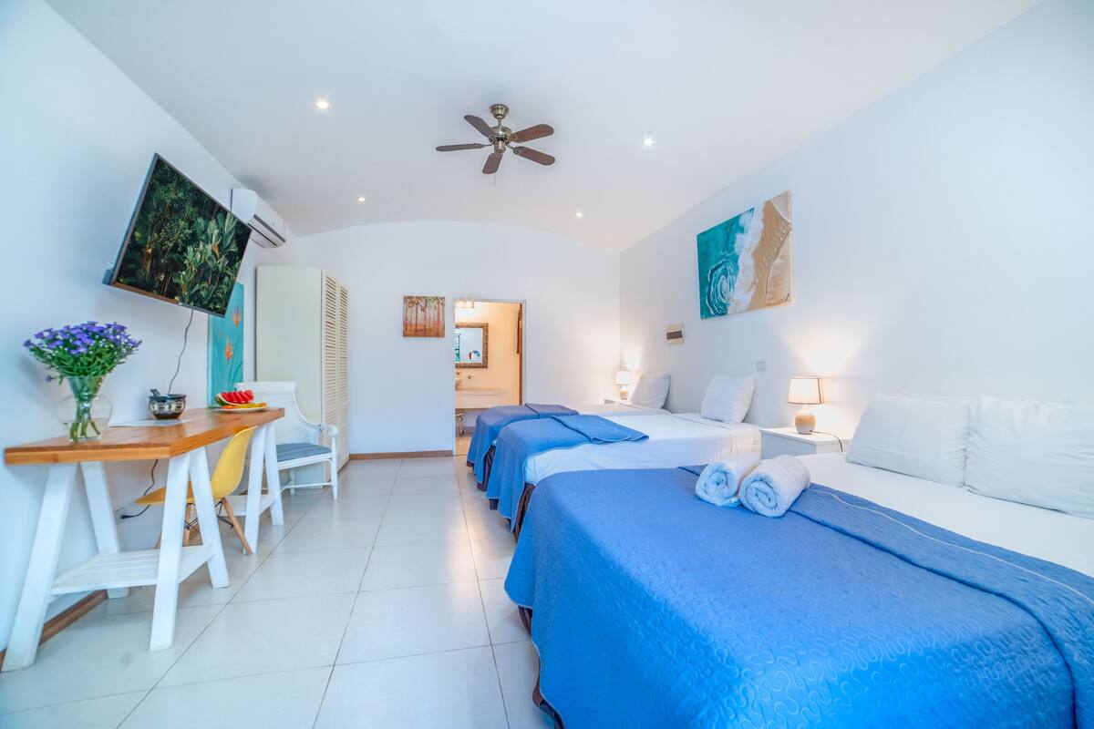 A hotel room with a bed, bedside tables, a desk with a chair, a TV, and artwork on the walls.