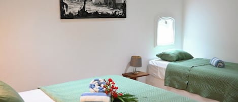 A room with two beds, a painting on the wall, a window, and a nightstand with a lamp.