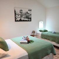 Una habitación con dos camas, un cuadro en la pared, una ventana y una mesita de noche con lámpara.