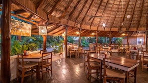 Ein Restaurant im Freien mit Holztischen und -stühlen, einem Reetdach und Topfpflanzen.