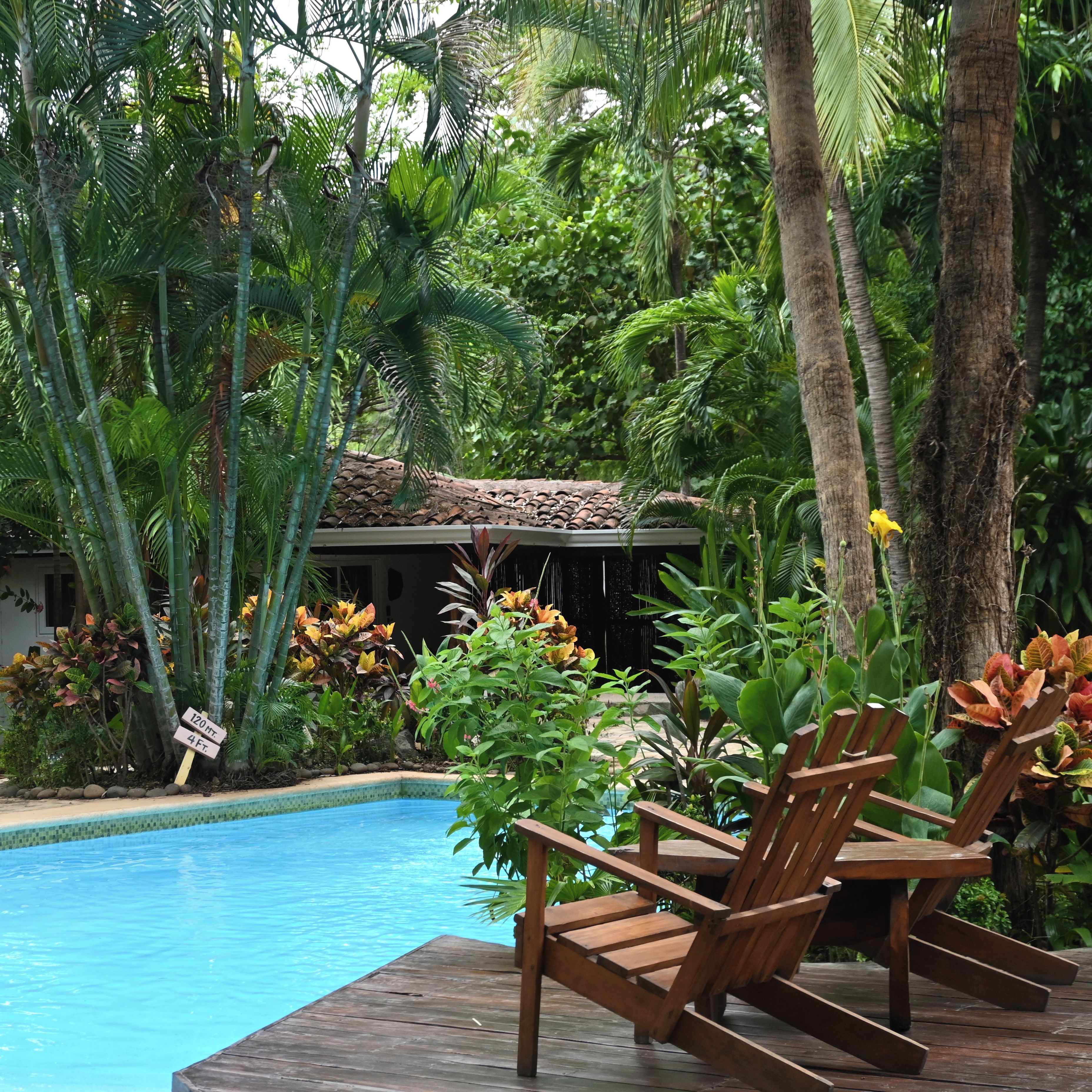 A pool area with wooden chairs and tropical plants.