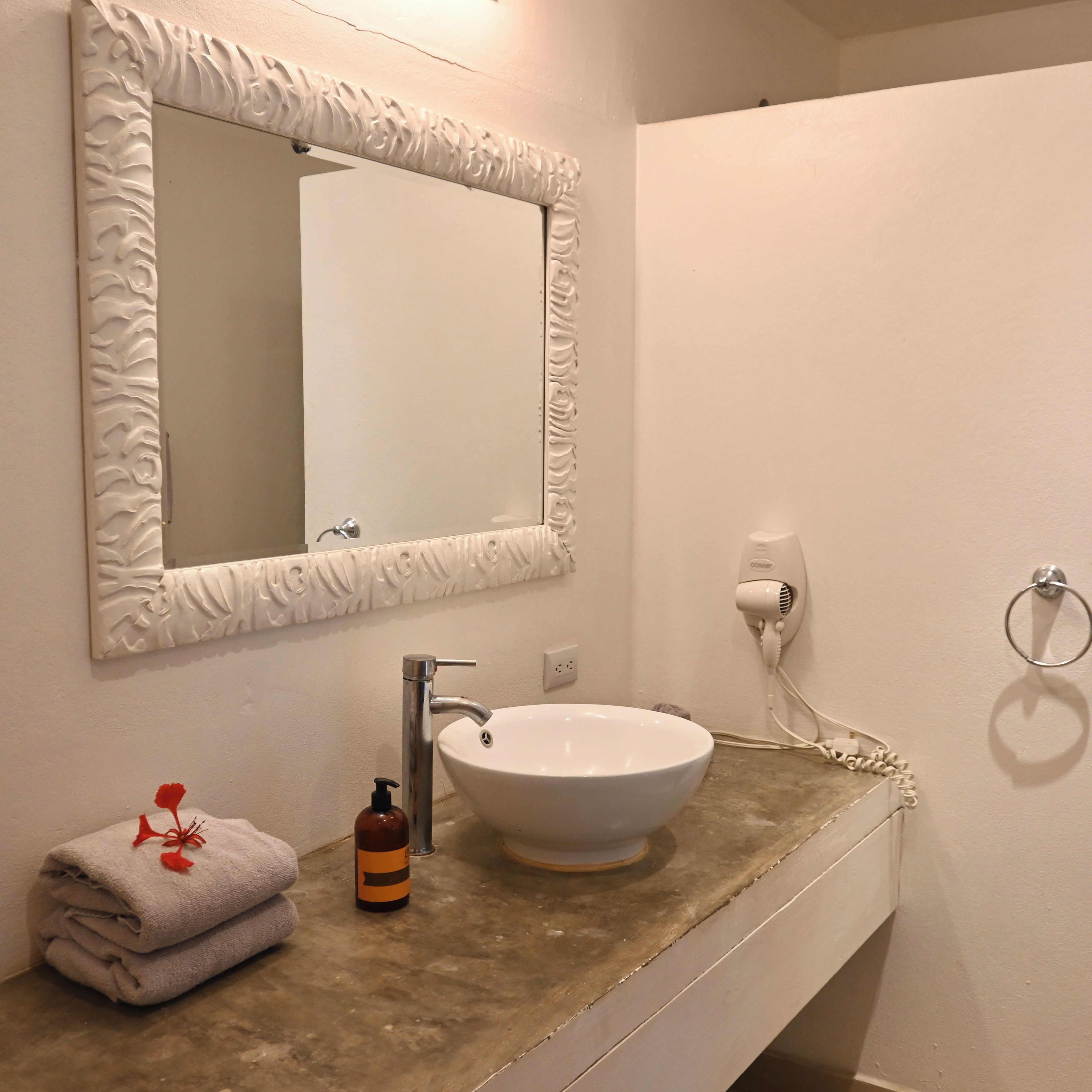A bathroom with a white sink, a mirror with a decorative frame, a towel rack, and a hairdryer on the wall.