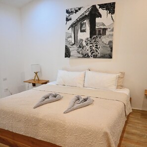 A bedroom with a bed, two pillows, a bedside table, a lamp, and a wall-mounted painting. - Hotel Pasatiempo (Tamarindo)
