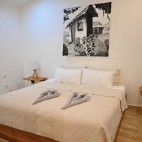 Un dormitorio con cama, dos almohadas, una mesita de noche, una lámpara y un cuadro colgado en la pared.