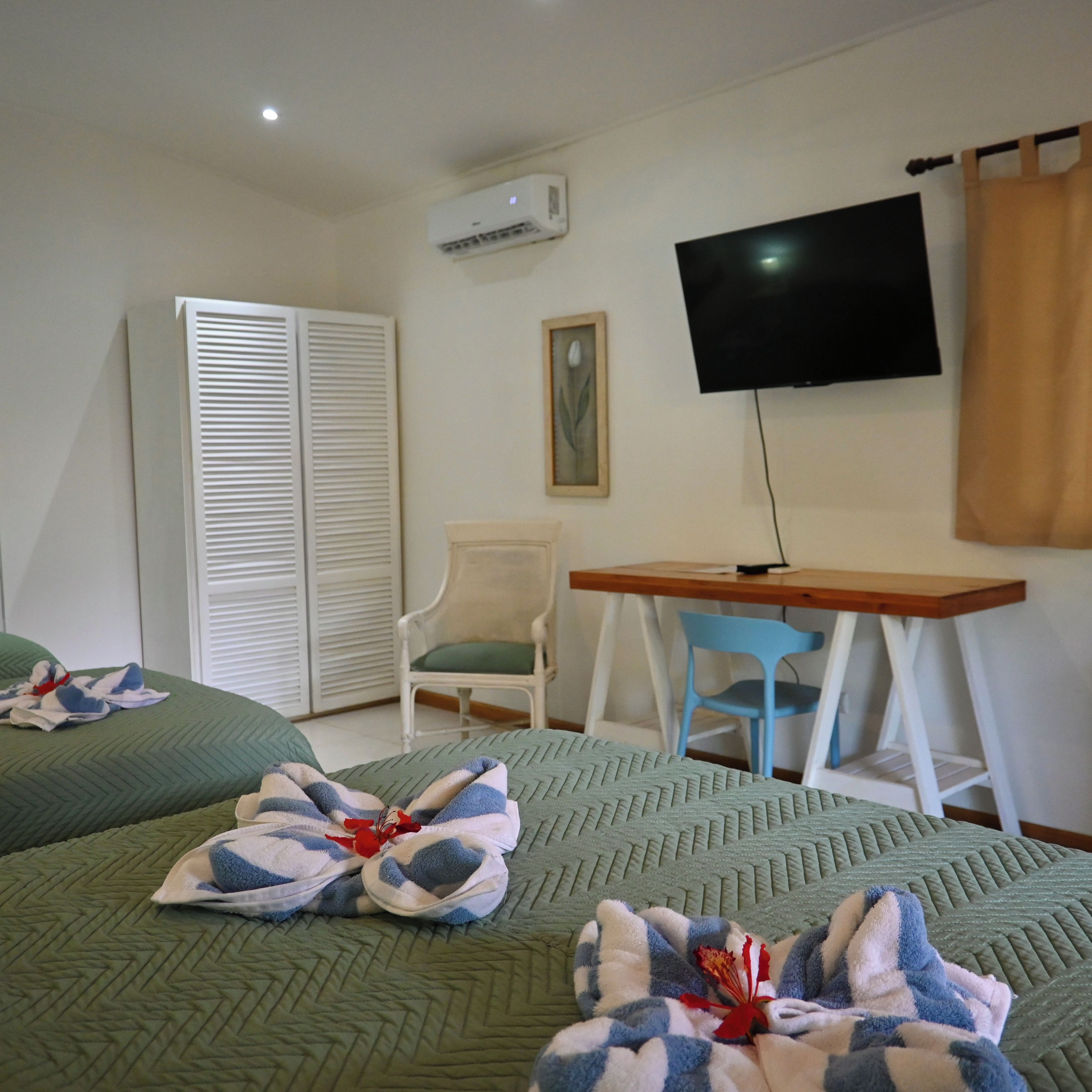 A hotel room with two beds, a desk, a chair, a television, and a wardrobe.