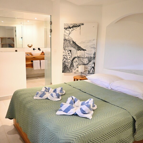 A hotel room with a bed, a painting on the wall, a bathroom with a mirror, and a sink.