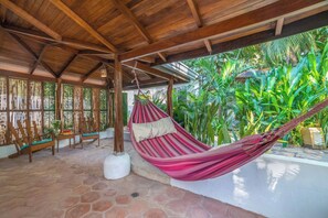 A hammock under a wooden roof, surrounded by plants and a stone floor. - Hotel Pasatiempo (Tamarindo)