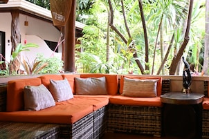 A room with a wicker sofa, a small round table, and a view of lush greenery outside.