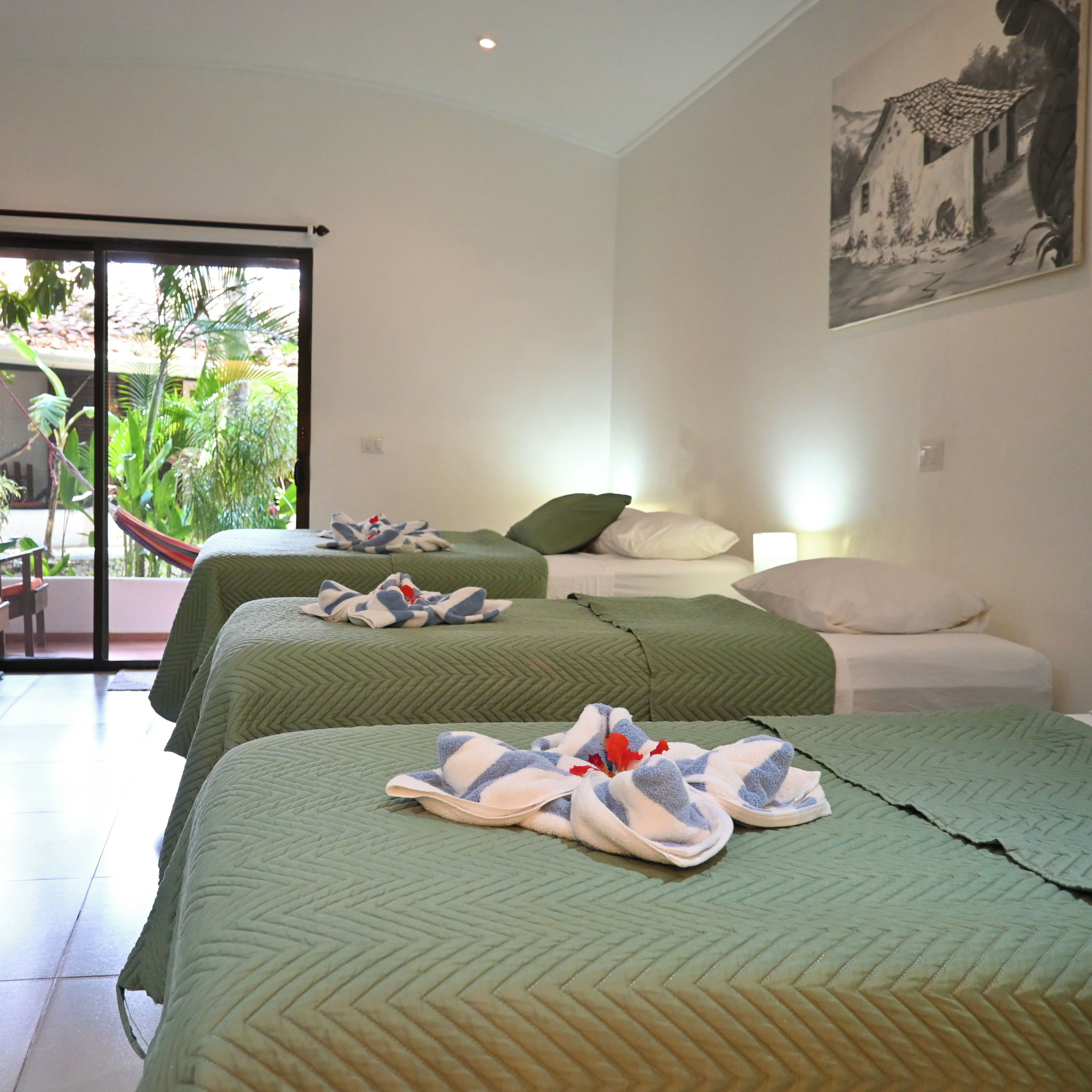A hotel room with two beds, a balcony with plants, and a painting on the wall.