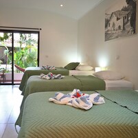A hotel room with two beds, a balcony with plants, and a painting on the wall.