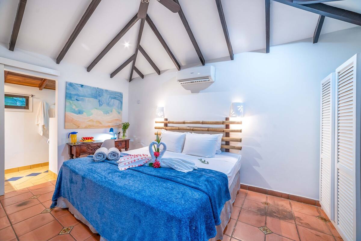 A bedroom with a bed, a blue bedspread, a wooden headboard, and a painting on the wall.
