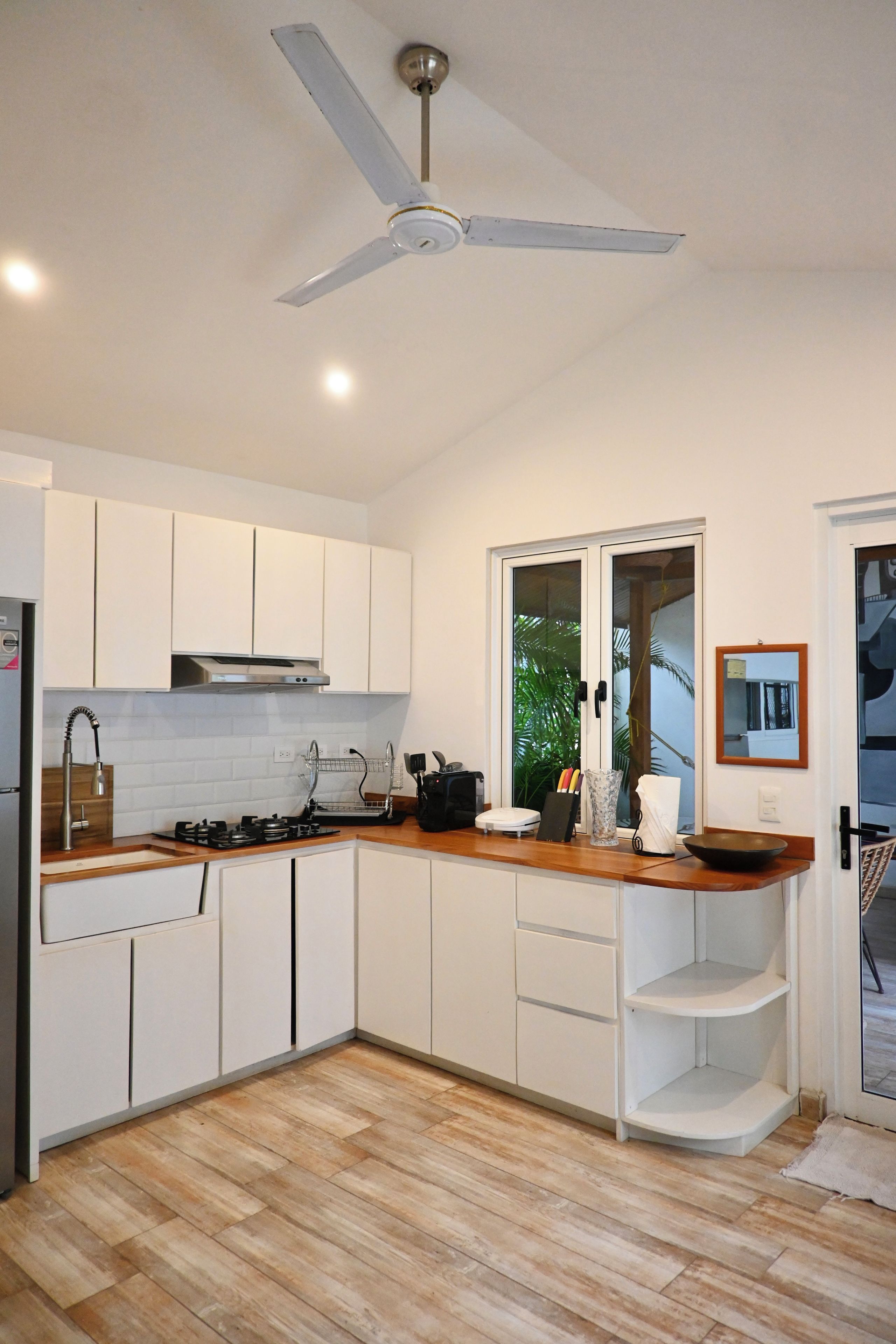 Una cocina moderna con armarios blancos, encimera de madera, estufa a gas y ventilador de techo.