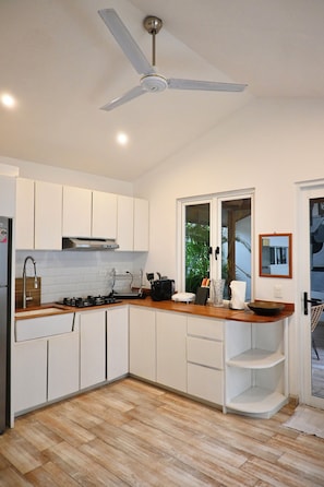 A modern kitchen with white cabinets, a wooden countertop, a gas stove, and a ceiling fan.