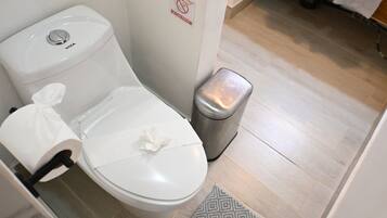 Un inodoro blanco con tapa, un cubo de basura y un cartel de 'no tirar basura' en la pared.
