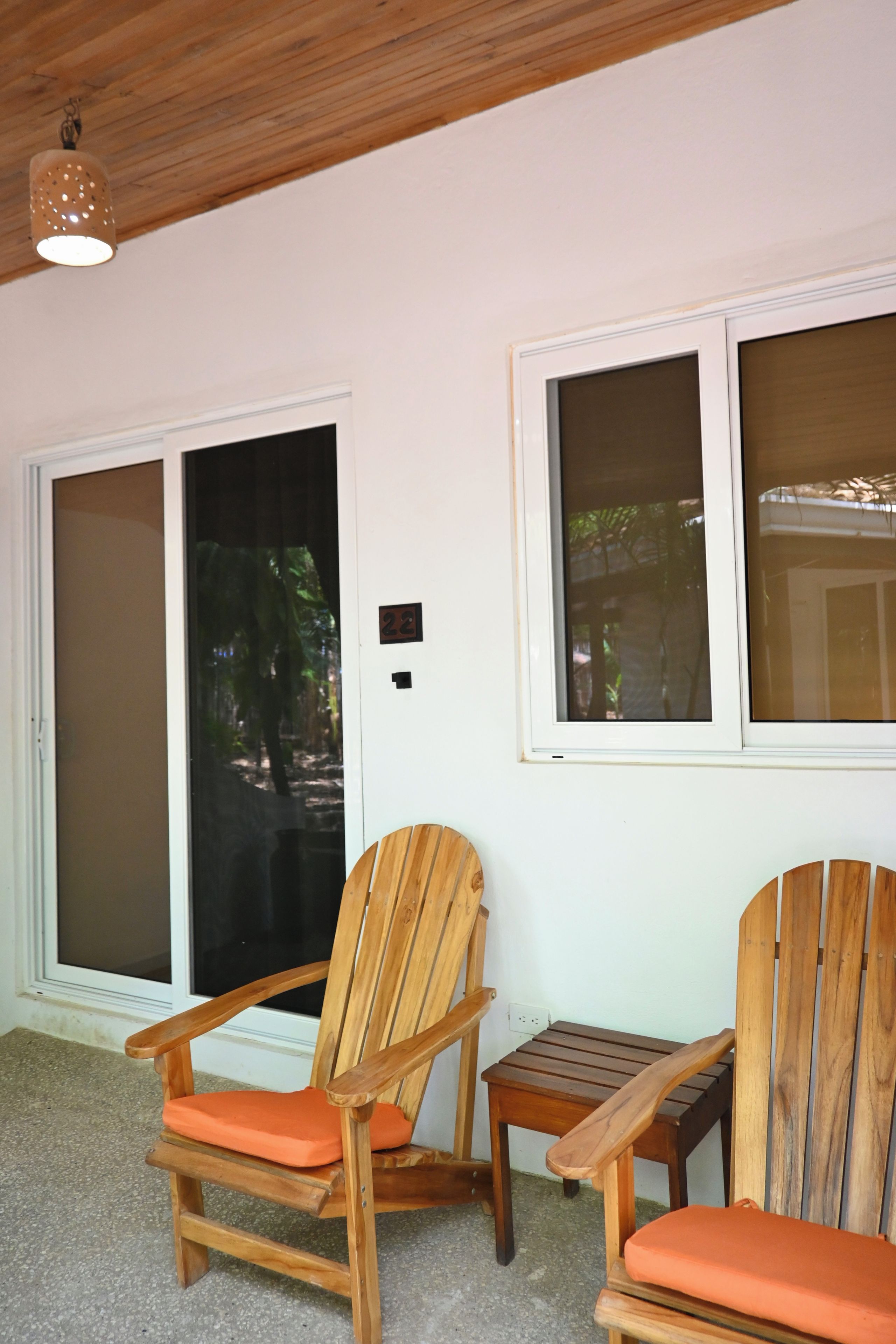 A room with two wooden chairs with orange cushions, a small wooden table, and a ceiling light fixture.