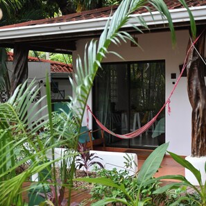 A covered outdoor area with a hammock, potted plants, and a sliding glass door leading to a room.