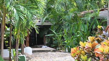 Un sendero de piedra serpentea a través de un exuberante jardín con diversas plantas tropicales y una edificación al fondo.