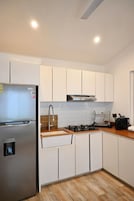 Una cocina moderna con gabinetes blancos, un refrigerador de acero inoxidable, una estufa a gas y un horno empotrado.