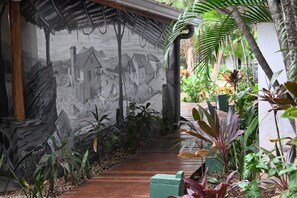 A pathway leading through a lush garden with a mural on the wall depicting a rural scene. - Hotel Pasatiempo (Tamarindo)