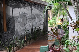 Un sendero serpentea por un exuberante jardín con un mural en la pared que muestra una escena campestre.