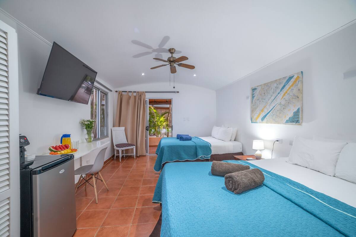 A hotel room with a bed, a desk with a refrigerator, a TV, and a ceiling fan.