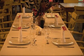 A dining table set with plates, cutlery, and wine glasses, with a vase of flowers in the center. - Hotel Pasatiempo (Tamarindo)