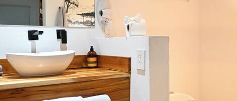 A bathroom with a wooden vanity, a white sink, a towel, a toilet, and a wall-mounted hairdryer.