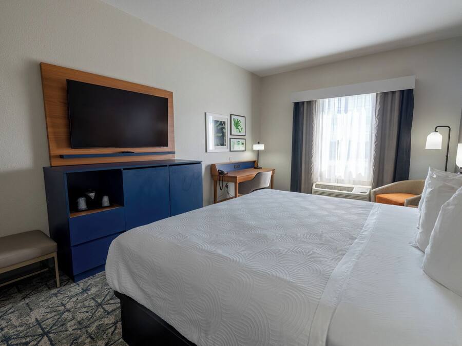 A hotel room with a large bed, a flat-screen TV mounted on a wooden cabinet, a desk with a chair, and a window with curtains.