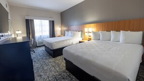 A hotel room with two beds, a desk, a chair, a lamp, and a window with curtains.