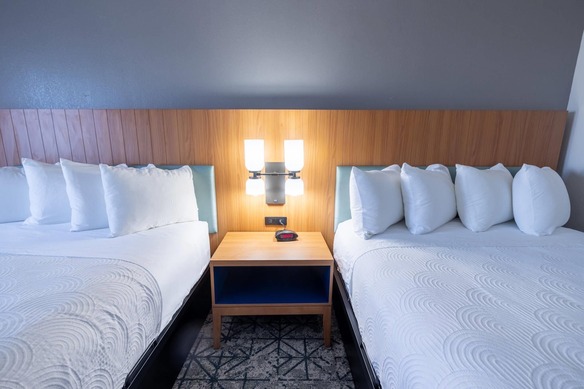 Une chambre d’hôtel avec deux lits, une table de chevet avec une lampe et une moquette à motifs.