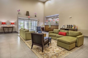 A lobby with a reception desk, green sofas, a patterned rug, and a chair. - Country Inn & Suites by Radisson, St. Petersburg - Clearwater, FL (Pinellas Park)