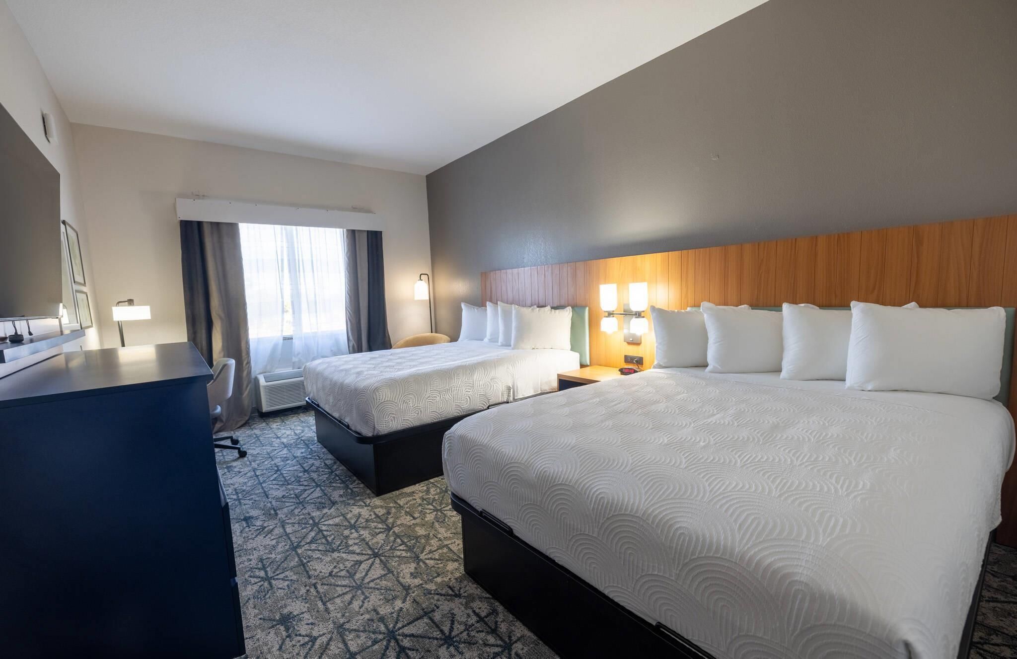 A hotel room with two beds, a desk, a chair, and a window with curtains.