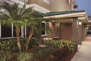 A modern building with a covered patio, brick walls, and a palm tree. - Country Inn & Suites by Radisson, St. Petersburg - Clearwater, FL (Pinellas Park)