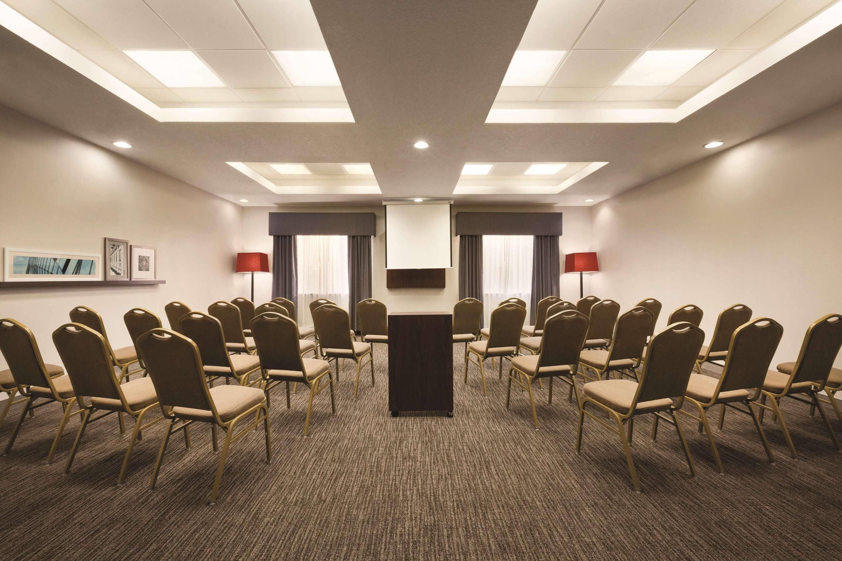 Un salón de conferencias con un atril central, filas de sillas y suelo alfombrado.