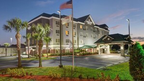 A multi-story hotel with a prominent American flag, a parking lot, and a landscaped entrance area.