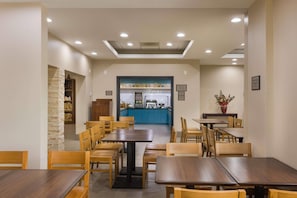 A restaurant with wooden tables and chairs, a blue counter, and a stone wall. - Country Inn & Suites by Radisson, St. Petersburg - Clearwater, FL (Pinellas Park)