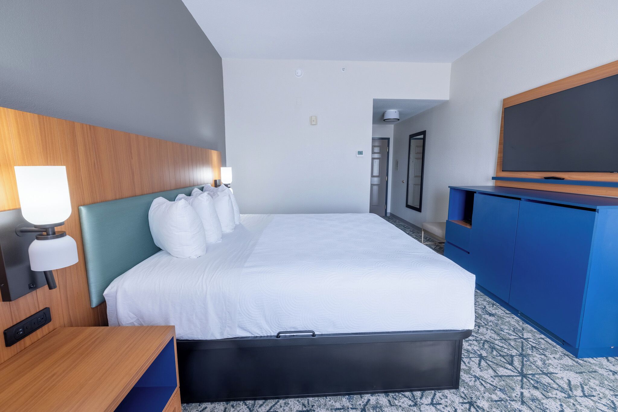 Una habitación de hotel con cama, escritorio, lámpara, televisor y armario.