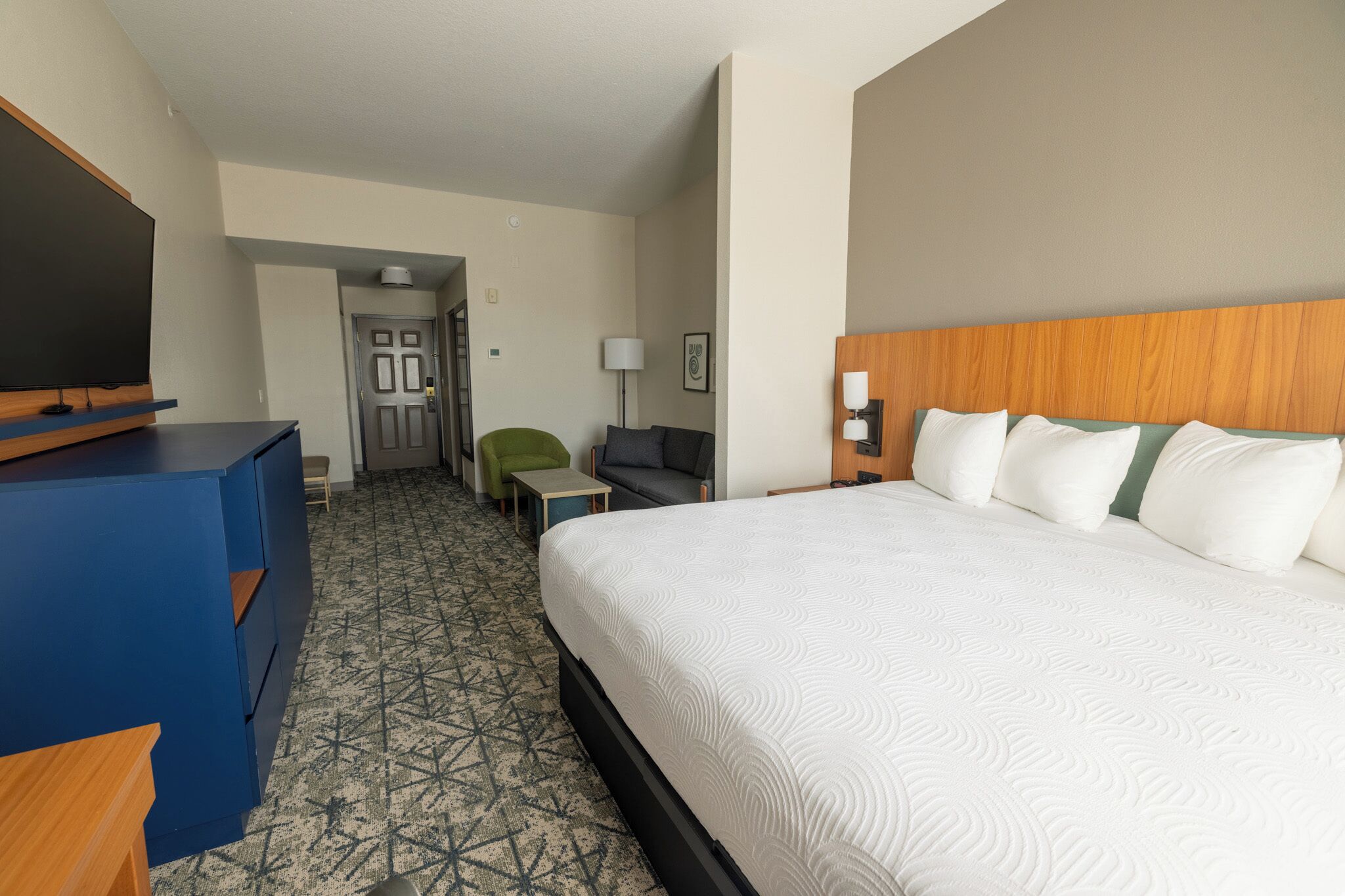 Habitación de hotel con una cama grande, un escritorio, una silla, un televisor y una puerta que da a otra habitación.