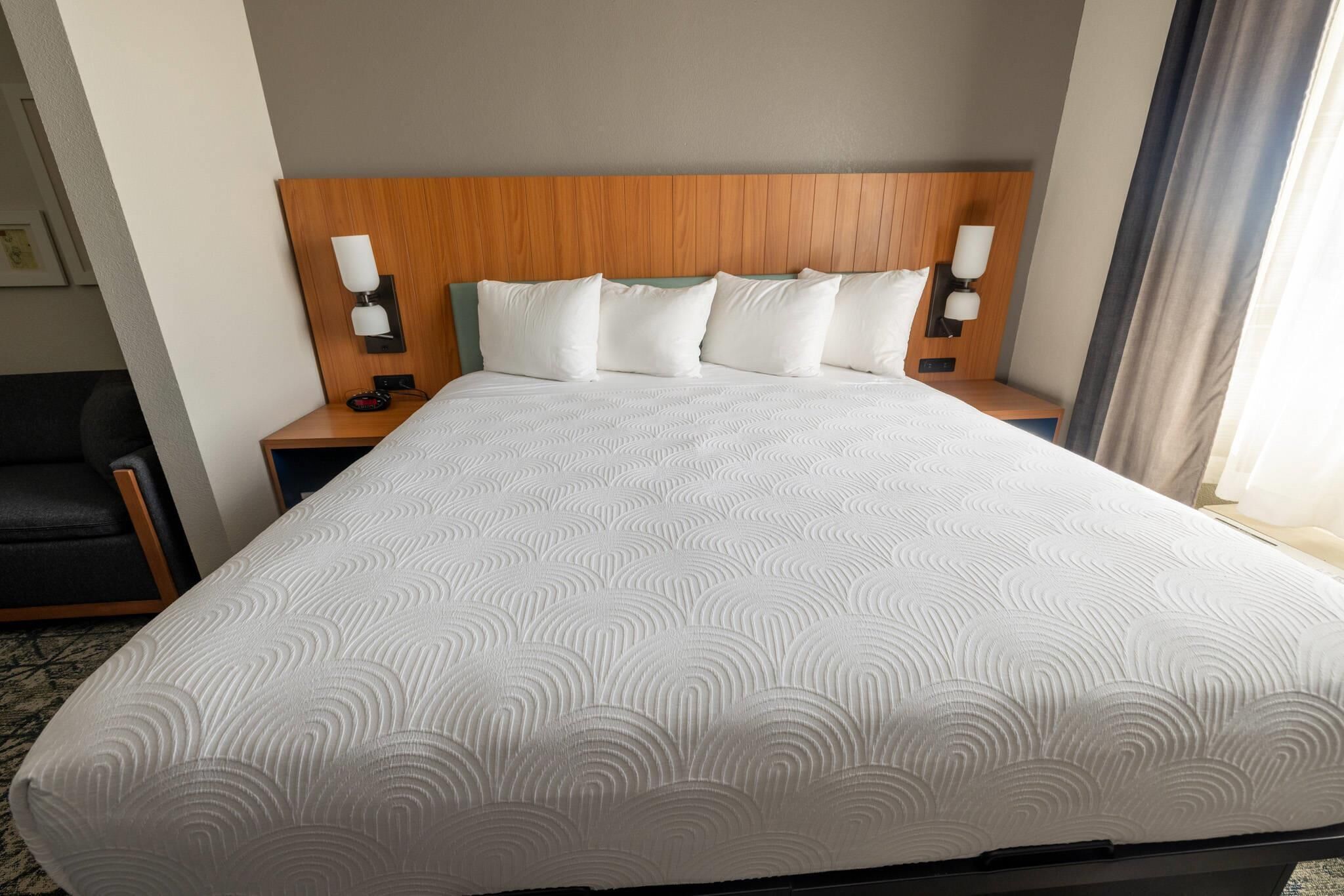 Een hotelkamer met een groot bed, een houten hoofdbord, twee nachtkastjes met lampen en een stoel.
