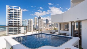 Une piscine sur le toit offrant une vue sur les toits de la ville, un espace repas avec des sièges en plein air, et un bâtiment blanc doté de grandes fenêtres.