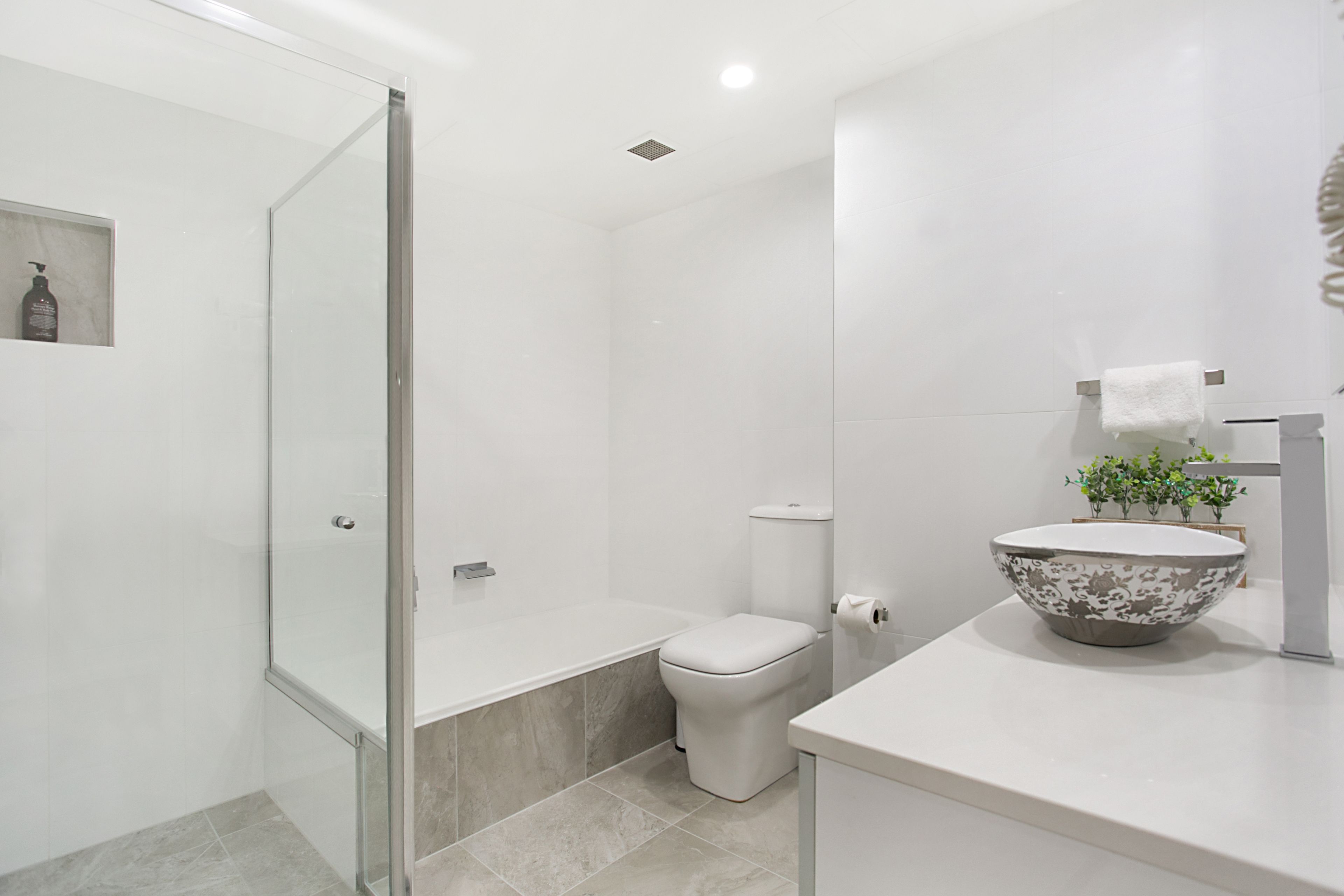 A modern bathroom with a glass shower enclosure, a toilet, and a sink with a decorative bowl.