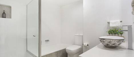 A modern bathroom with a glass shower enclosure, a toilet, and a sink with a decorative bowl.