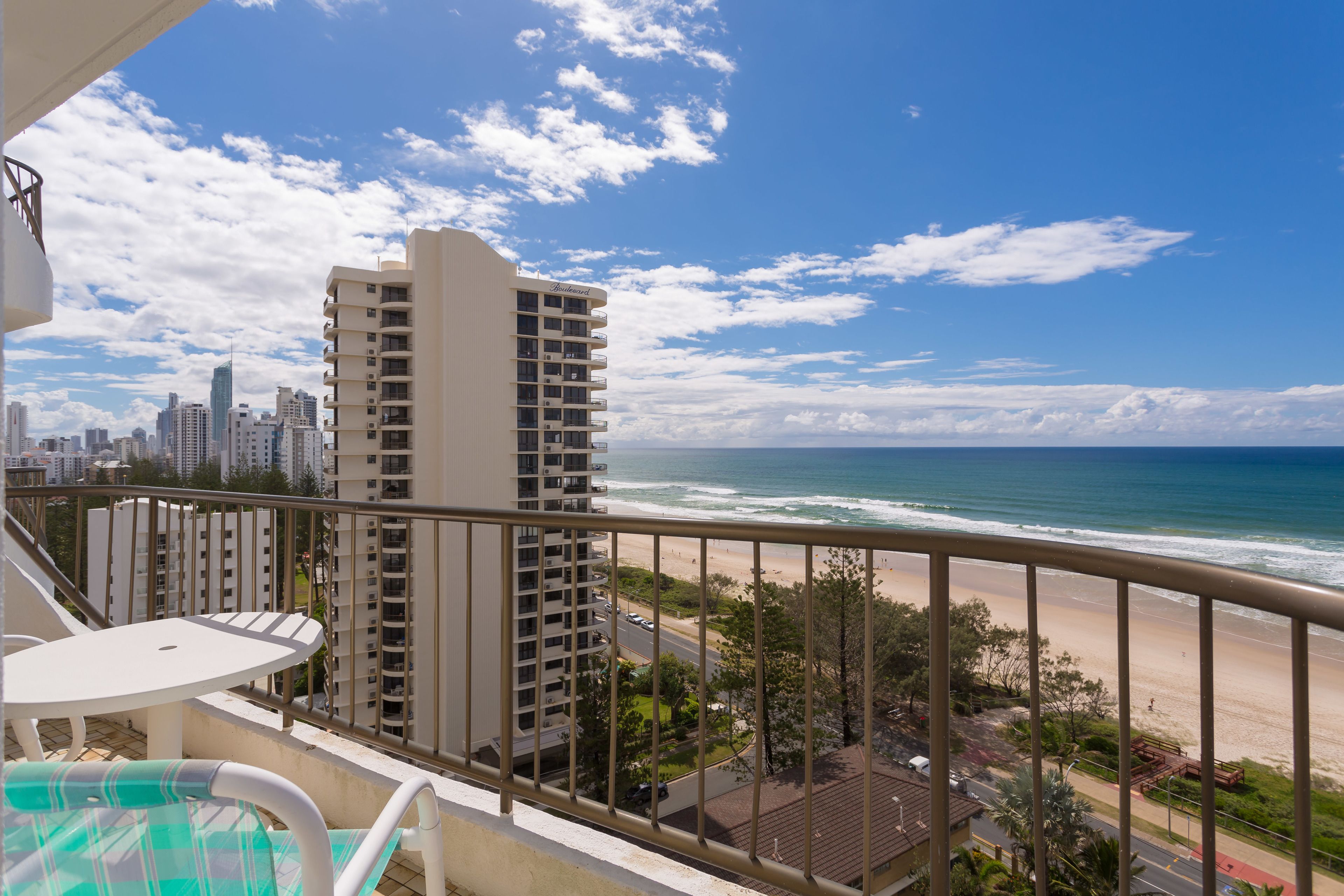 Un balcon avec vue sur la plage et l’océan, un immeuble de grande hauteur et un paysage urbain en arrière-plan.