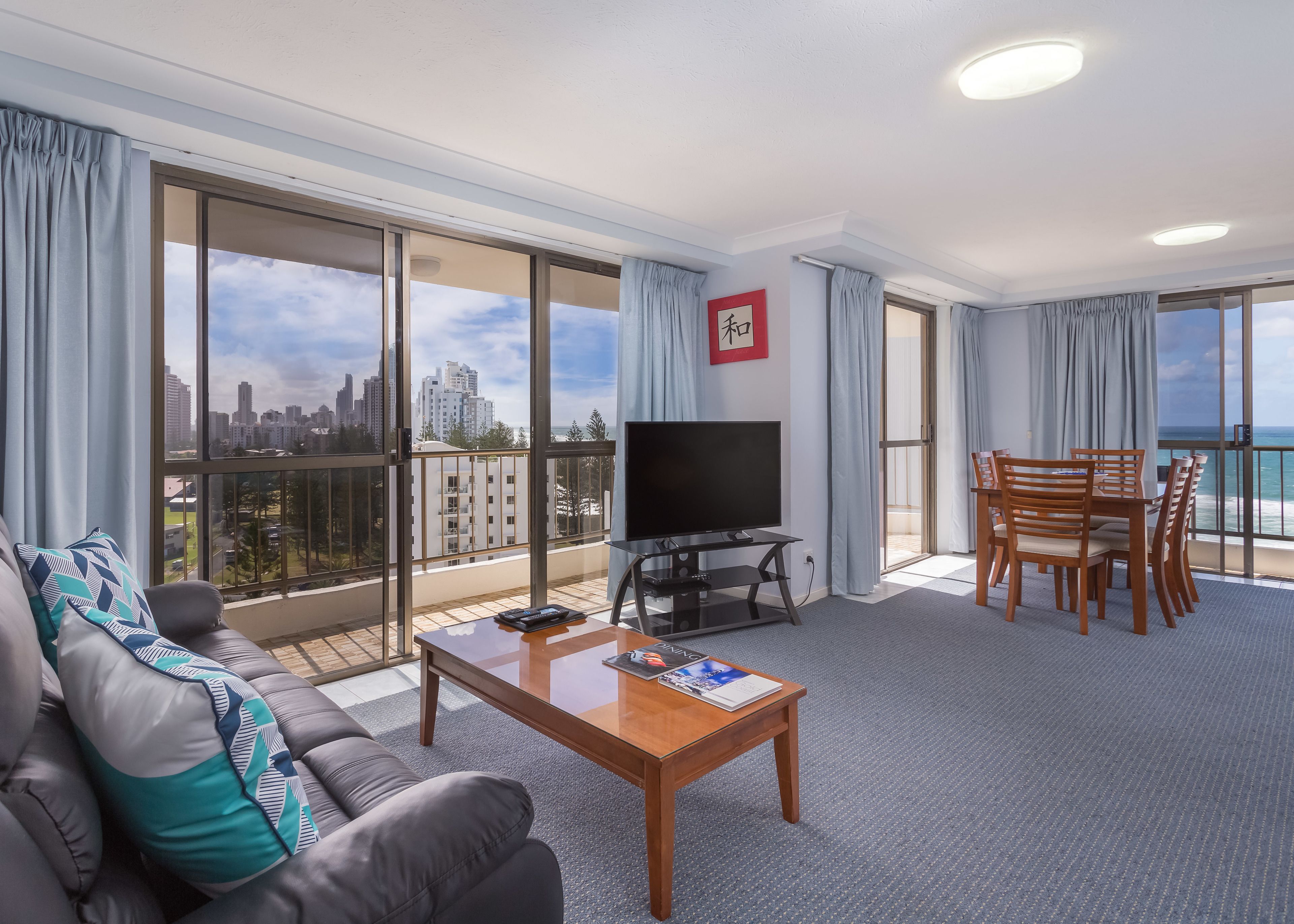 Een moderne hotelkamer met balkon, flatscreen televisie, houten eettafel en een bank met gestreepte kussens.